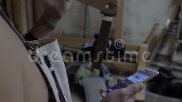 一个穿着工作围裙的木匠通过手机中的应用程序设置了一个照片装置人通过摄像机控制摄像机视频的预览图
