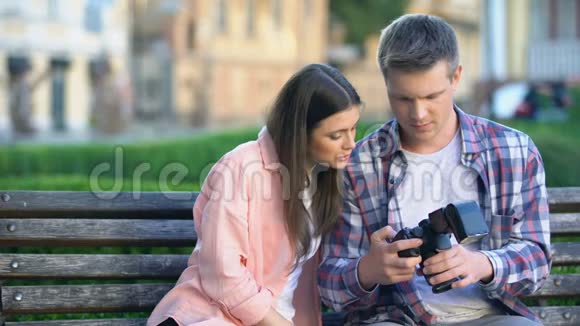 年轻夫妇坐在长凳上用相机观看旅游旅行的照片视频的预览图