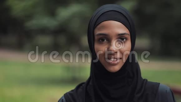 快乐的年轻音乐女孩的肖像戴着Hijab微笑站在公园背景特写视频的预览图