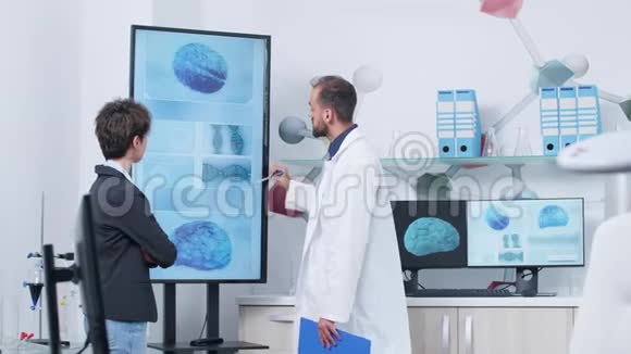穿着白色长袍的医生在医学研究机构向病人展示三维大脑模拟视频的预览图