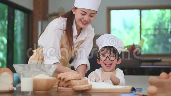 可爱的小亚洲男孩和美丽的母亲在家里厨房的桌子上筛面团粉准备烘焙面包店和蛋糕a视频的预览图