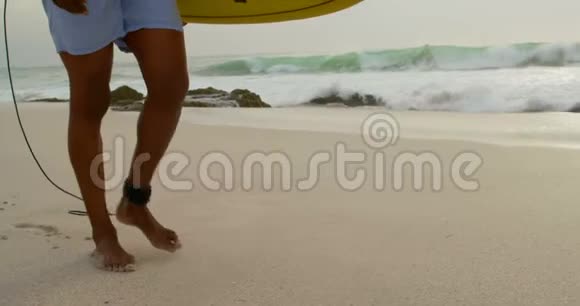 在海滩上用冲浪板行走的非裔美国男性冲浪者的侧面景色视频的预览图