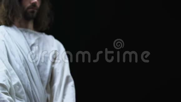 穿着长袍的耶稣在镜头前展示圣经信仰和信仰黑暗的背景视频的预览图