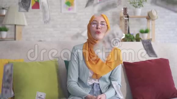 积极的年轻穆斯林妇女在家里坐在沙发上抓着钞票视频的预览图