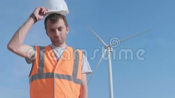 端口近景拍摄的成年工程师穿着橙色背心和白色安全帽背景上有风力涡轮机视频的预览图