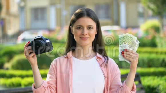 女性在镜头前展示相机和一堆欧元赚钱的职业视频的预览图