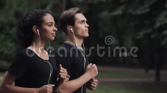 漂亮的年轻夫妇戴着耳机看着轻松的跑步在公园侧景特写女孩在左边视频的预览图
