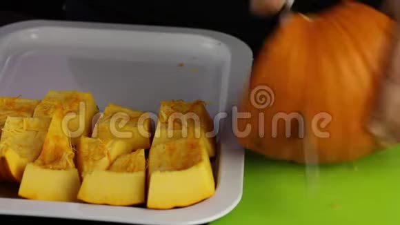 一个男人把一个橙色的南瓜切成碎片一片南瓜躺在托盘上世界素食日视频的预览图