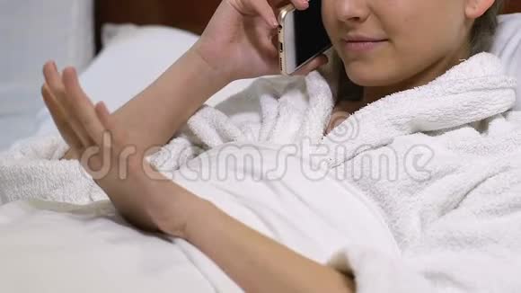 漂亮的年轻女性穿着浴袍在电话中聊天躺在床上温泉酒店视频的预览图