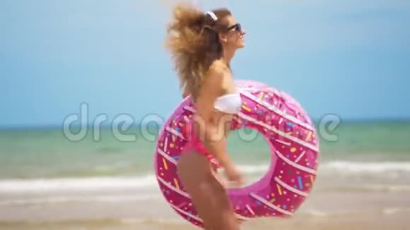 年轻女子慢跑与充气甜甜圈与充气戒指在海滩上视频的预览图