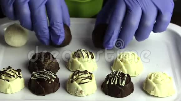 一个戴着橡胶手套的人把糖果成排放在托盘上白色和黑色巧克力的釉面糖果视频的预览图