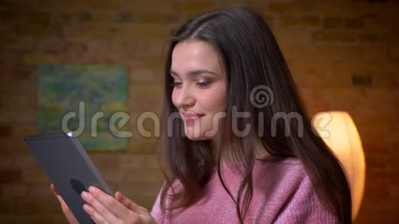 在一间舒适的公寓里年轻漂亮的黑发白种人女性在平板电脑上留言开心地笑着特写镜头视频的预览图