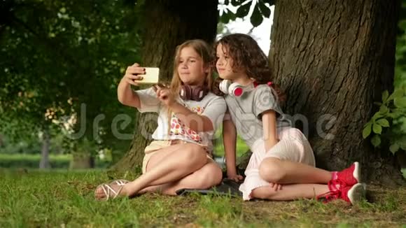 美丽快乐的女孩姐妹学生坐在公园户外草地上他们正在休息正在自拍视频的预览图