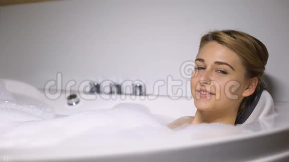 微笑的女人在按摩浴缸里放松看相机水疗美容程序视频的预览图