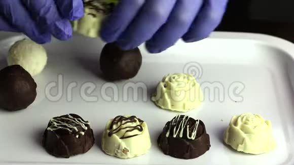 一个戴着橡胶手套的人把糖果排成一排放在托盘上白色和黑色巧克力的釉面糖果视频的预览图