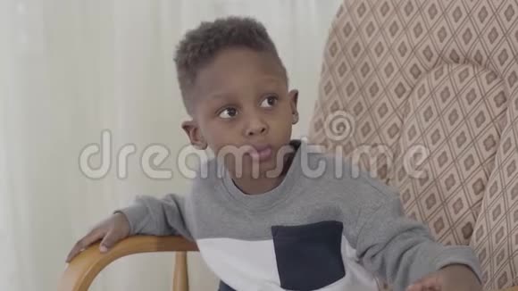 有趣的非裔美国男孩嚼口香糖或糖果露出舌头坐在扶手椅上的肖像视频的预览图