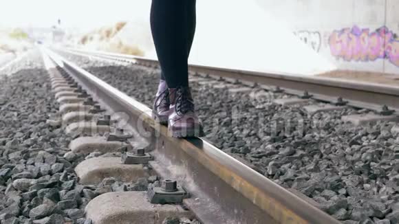 穿着紫色靴子的年轻女子在火车轨道上行走保持平衡在背景下满是涂鸦的隧道视频的预览图