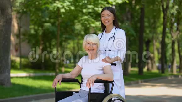女护士和残疾老年妇女对着镜头微笑在医院公园放松视频的预览图