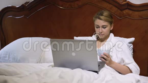 年轻商务女性在床上喝咖啡在笔记本电脑上工作项目视频的预览图