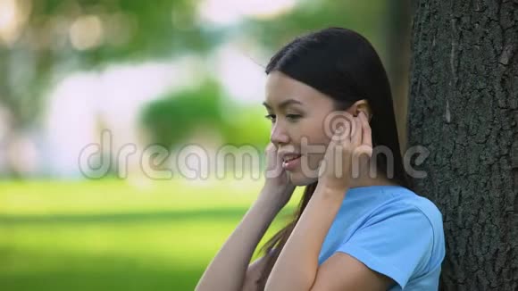戴无线耳机听音乐的微笑女性坐在公园里视频的预览图