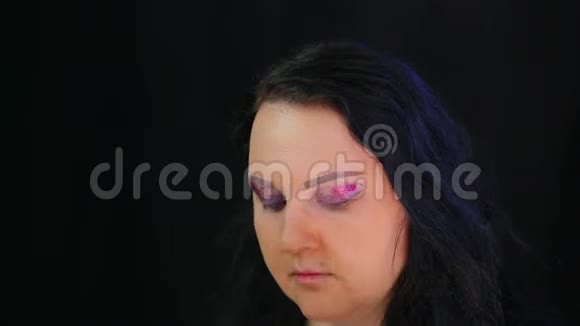 一个深色的女人在她的眼皮上涂上明亮的阴影和紫色的火花时光飞逝视频的预览图