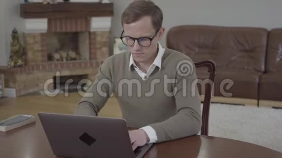 年轻谦逊的戴着眼镜的人坐在办公室的木桌旁用笔记本电脑工作无法辨认视频的预览图