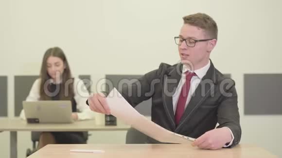 自信的年轻男经理穿着西装坐在前台的办公桌前看着镜头年轻漂亮视频的预览图