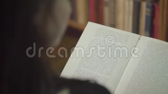 在图书馆里读一本书的年轻学生的后视图女孩正站在书页前面翻书视频的预览图