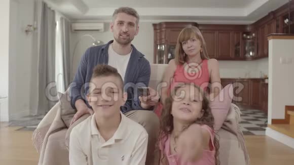快乐的年轻家庭一起坐在家里看电视父亲拿着遥控器打开频道视频的预览图