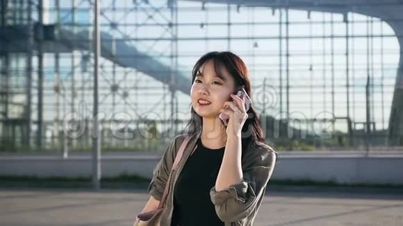 在机场建设的背景下令人愉悦的亚洲年轻女性在智能手机上交谈视频的预览图