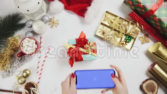 女士双手拍照圣诞礼物在白色桌子上铬键手机显示视频的预览图