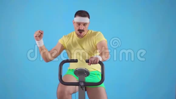 有目的的80运动员带着胡子骑在蓝色背景的慢动作的自行车上视频的预览图