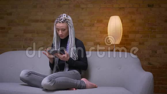 一位年轻迷人的白种人时髦女性在平板电脑上的特写镜头她坐在舒适的室内沙发上浏览视频的预览图