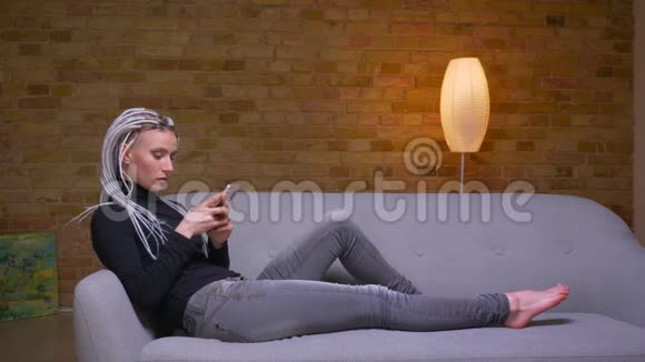 特写侧景拍摄年轻迷人的白种人潮女使用手机躺在室内沙发上视频的预览图