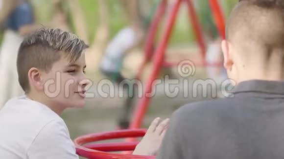 两个兄弟坐在公园里聊天女人在后台摇摆男孩视频的预览图