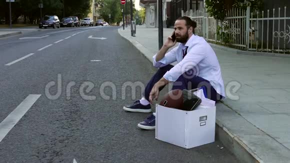 被解雇了一位穿着正式服装的英俊商人坐在人行道上手里拿着一盒私人物品和视频的预览图