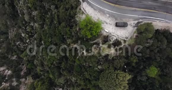 Drone在一条弯弯曲曲的路上用一片绿油油的灌木和一辆停在路边的黑色轿车向一个长满树木的山坡射击视频的预览图