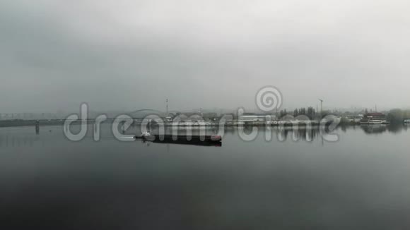 在市中心的工业烟雾中铁驳船在空旷平静的河流上航行在市区的一座桥上飘浮着一片大雾视频的预览图