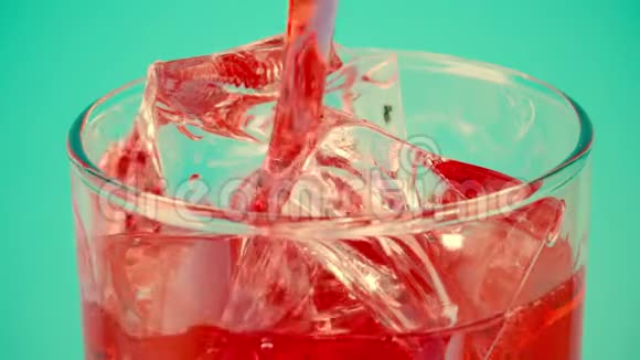 将红色软饮料倒入盛满冰块的玻璃杯中置于青色背景下特写慢动作拍摄红色视频的预览图