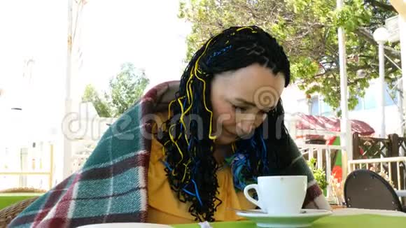 一位年长的女士身披格子布坐在一家夏季户外咖啡馆里视频的预览图