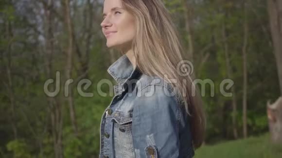 漂亮的女人带着手机穿着白色长裙和牛仔裤夹克走在森林的近处摄像机从视频的预览图