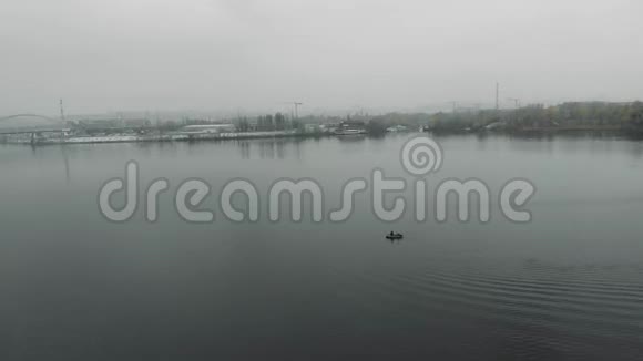 小孤独的渔船漂浮在烟雾弥漫的工业中心附近宽阔平静的河流上渔夫在河上钓鱼视频的预览图