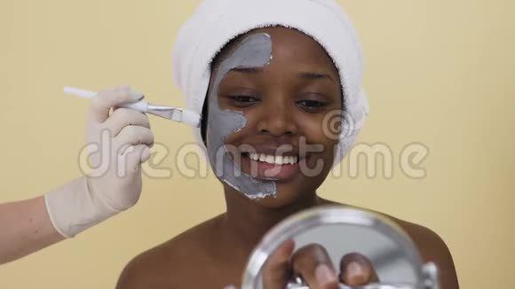 美容师用手在水疗沙龙里给年轻的非裔美国妇女敷面膜视频的预览图