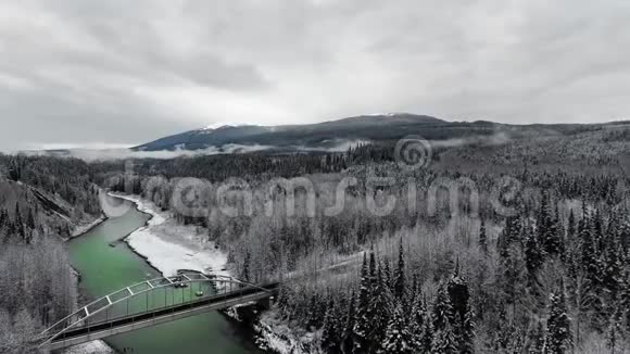 在白雪皑皑的山脚下茂密的松林中Drone在一条翡翠河上卸下一座路桥视频的预览图