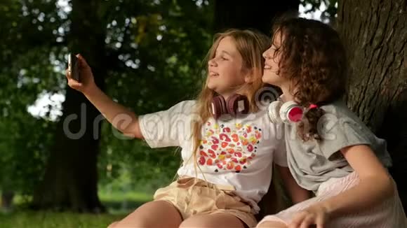 美丽的快乐女孩姐妹学生坐在公园户外草地上他们正在休息自得其乐视频的预览图