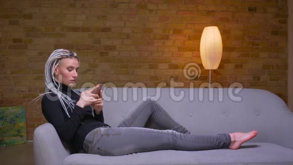 特写侧景拍摄年轻迷人的白种人潮女使用电话悠闲地坐在沙发上视频的预览图