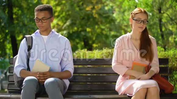 多种族学生手牵手坐在公园的长凳上第一次约会极客视频的预览图