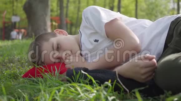 春天公园里一个可爱的男孩躺在绿草上的肖像户外娱乐活动视频的预览图