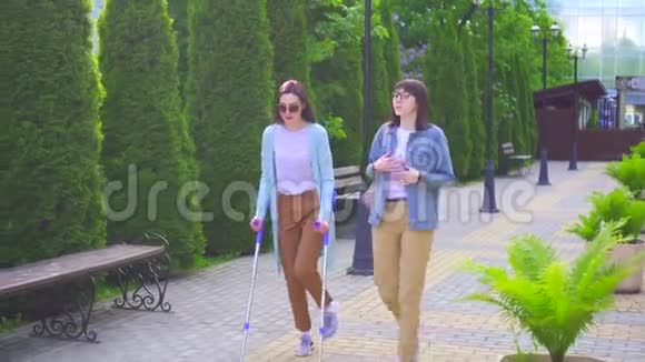 一位拄着拐杖受伤的年轻残疾妇女和一位朋友一起微笑着慢慢地交谈视频的预览图