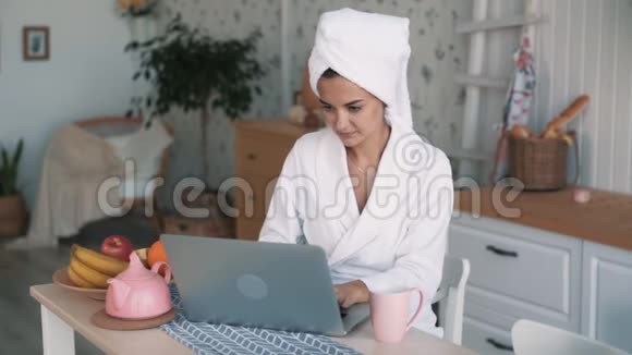 穿白色浴袍的女孩头上有毛巾在笔记本电脑上工作慢动作视频的预览图